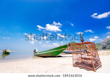 Wooden cage with bird on white sand beach, Thailand.