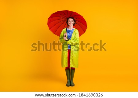 Full length photo portrait of smiling woman standing under holding umbrella with two hands isolated on bright yellow colored background