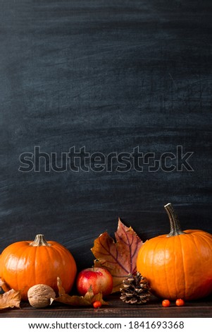 Pumpkin, fallen yellow leaves apples and nuts, on table, chalkboard. Template for design. The concept of autumn mood, halloween and Thanksgiving.