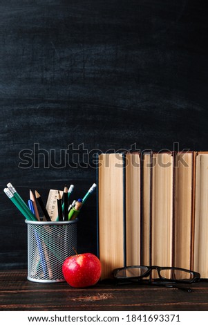 Teacher's table, books, pencils, pens, glasses and an apple, on chalkboard background. Copy space.