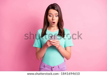 Photo portrait of shocked woman holding phone in two hands isolated on pastel pink colored background
