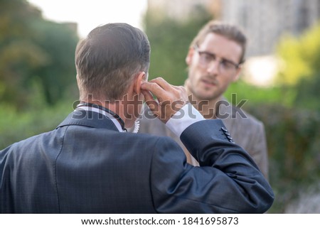 Journalist job. Rear view of male journailst fitting earpiece, his male colleague helping him