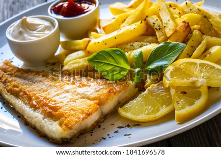Fish dish - fried cod fillet with French fries and vegetable salad on wooden table 