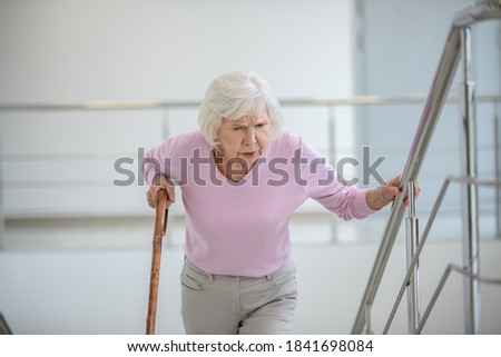 Tired. Elderly woman with a walking stick slowly going upstairs Royalty-Free Stock Photo #1841698084