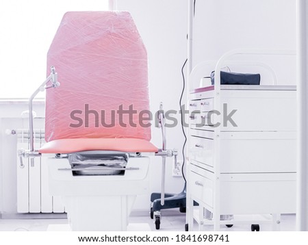 Red procedural medical chair and white bedside table on wheels boxes with drawers in light interior of doctor's office. Workplace