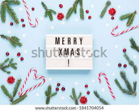 Christmas winter holiday composition. Merry Christmas text on lightbox, Xmas candy canes, Fir tree branches, pastel blue background. Flat lay, top view, copy space. Holiday card mockup template.
