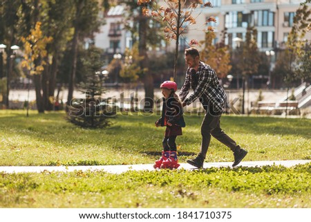 Dad and daughter roller-skate in the park. Leisure weekend together.