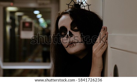 Close-up of a zombie girl with long hair and matching makeup looking around the corner with an interested face. Halloween Eve. October holiday. Royalty-Free Stock Photo #1841726236