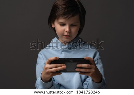 Portrait of Cute boy 10-12 years old, dressed in casual clothes, standing with gamepad in hands and playing video game. Childhood, facial expression concept. Studio shot, gray background
