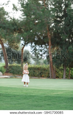 Cute little 1 year old girl standing on grass next to tree in fairy tale forest. holding little yellow flower.