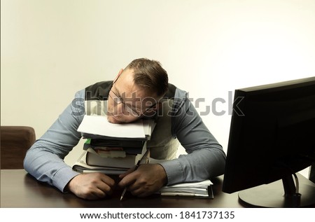 A man sleeps in the workplace on a pile of paper. Office worker sleeps on the table