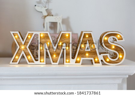 Vintage wooden word "Xmas" with lights on the shelf. New year decorations in rustic style. Wooden letter on white background. Lantern in view of the word "XMAS", classic Christmas decore  Royalty-Free Stock Photo #1841737861