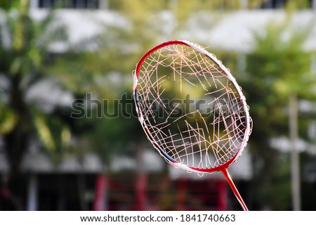 Badminton racket which has broken string inside frame with natural blurred background.