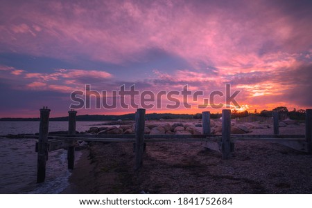 Storm damaged dock at the beach with pink and orange sunset clouds