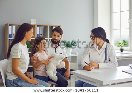 Happy family with child in pediatrician's office consulting friendly young female doctor. Mother, father and daughter talking to supportive paediatrician during regular check-up in modern hospital Royalty-Free Stock Photo #1841758111