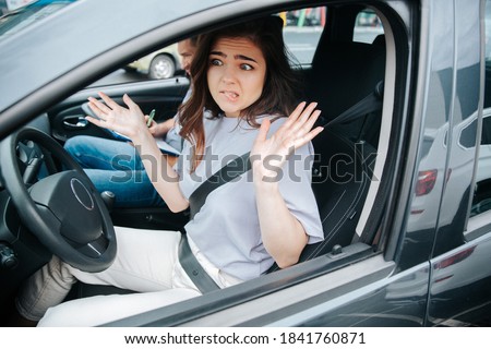 Lovely young woman is troubled with results of driving lesson. Attractive confused woman shrugs up or makes a helpless gesture after making a mistake. Novice driver concept. Royalty-Free Stock Photo #1841760871