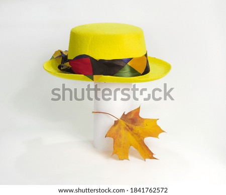 Yellow clown hat on a stand and autumn maple leaf on a light background.