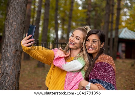 Two beautiful friends taking selfie in the forest 