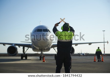 The runway traffic controller uses gestures and sticks to help the aircraft choose the correct trajectory around the airfield. Wearing a reflective vest