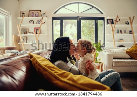 Playful young woman kissing toddler girl while sitting on sofa at home