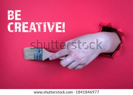 BE CREATIVE. Painter's brush in a woman's hand. Red paper background