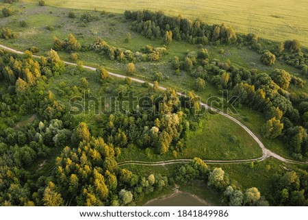 Aerial view of rural road between green field and forest. European nature.