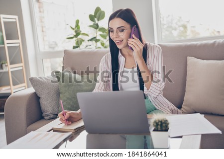 Photo of young busy business woman sit couch tell telephone write pencil diary wear glasses shirt in home workstation indoors
