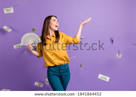 Photo of young lady raise arm hold fan cash fall money wear yellow shirt blue pants isolated violet color background