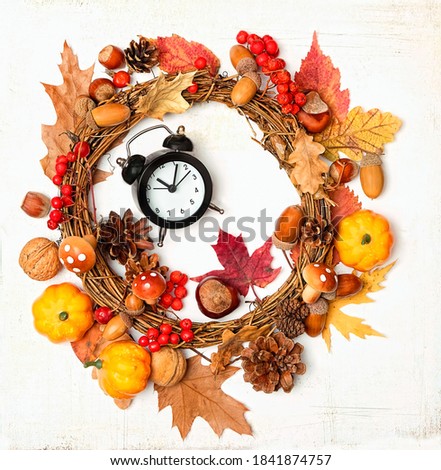 Autumn wreath with bright leaves, acorns, cones, berries and alarm clock on abstract light background. fall season concept. flat lay