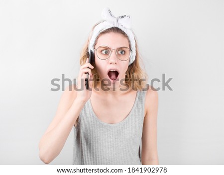 Portrait of a shocked young casual blonde woman talking on mobile phone isolated over white background