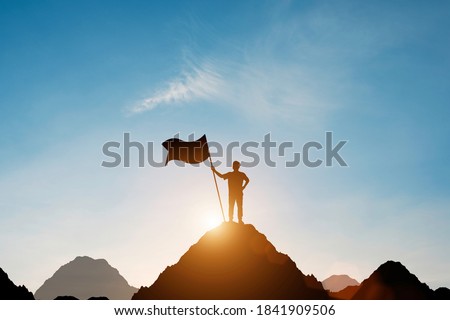 Silhouette of businessman holding flag on the top of mountain with over blue sky and sunlight. It is symbol of leadership successful achievement with goal and objective target. Royalty-Free Stock Photo #1841909506