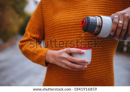 A young tourist woman drinks a hot drink from a cup and enjoys the scenery in the mountains. Trekking concept, Warm autumn weather, calm scene. Wanderlust photo series.