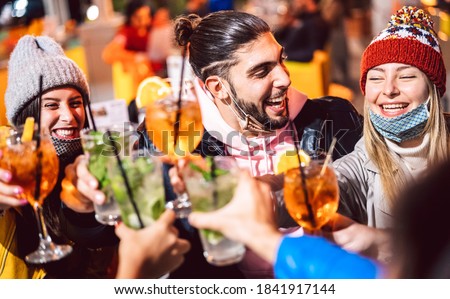Happy friend toasting fancy drinks at night bar with open mask - New normal lifestyle concept with milenial people having fun together on winter clothes at apreski - Focus on guy face