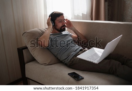 Man on sofa with headphones and notebook at home. young hipster wear headphones study online watching webinar podcast on laptop listening learning education course or music, elearning concept