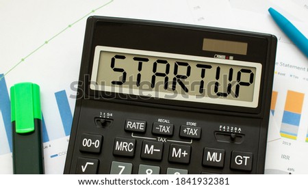 A calculator labeled STARTUP lies on financial documents in the office. Business concept