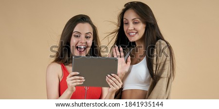 Two Happy young women using tablet for video call isolated on beige background