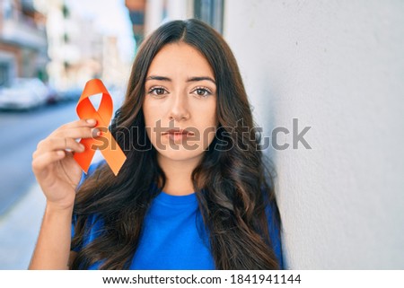 Young hispanic woman with serious expression holding orange ribbon at the city. Royalty-Free Stock Photo #1841941144