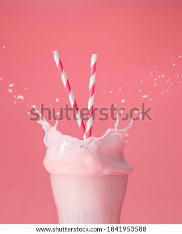 striped straws in a glass of splashing strawberry milkshake isolated on pastel pink color backdrop Royalty-Free Stock Photo #1841953588