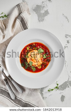 Salmon fish cake with tomato sauce and fresh greens. White bowl on rustic table with cloth. Gourmet food concept