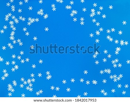 Scattered white snowflakes on a blue background. Simple flat lay with copy space. Stock photo.