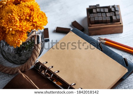 Empty open craft notebook and orange chrysanthemum flowers on rustic background. Greeting card with copy space for your text