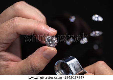 Round shape diamond in hands of jeweller. Man jeweller examines a diamond. Gem grading and checking. Diamond business. Royalty-Free Stock Photo #1842027367