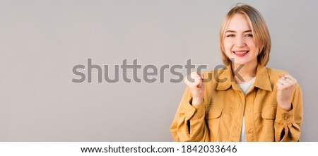 Surprised happy blond woman rejoices and looking at the camera over gray background