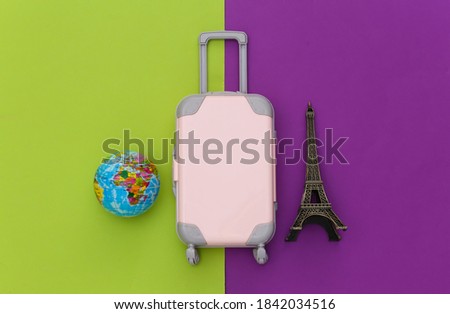 Traveled to Paris. Mini plastic travel suitcase, passport and statuette of the Eiffel Tower, globe on green purple background. Top view. Flat lay