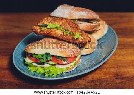 Assorted delicious baguette sandwiches filled with thinly sliced ham or salami and fresh green lettuce or basil arranged in an oblique row on an old wooden table