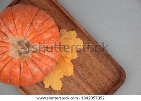 Pumpkin and yellow autumn leaves on wooden plate against gray background flat lay. Image contains copy space
