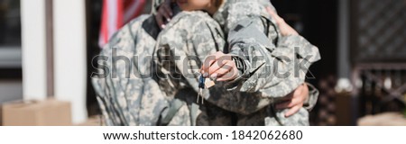 Cropped view of keys with blurred military couple embracing on background, banner