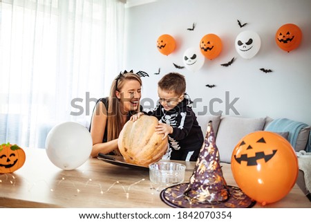 Mother and son carving pumpkin for Halloween holiday. Getting ready for Halloween. Family bonding during Halloween. Mother and son playing together during Halloween night