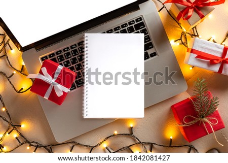 Mock up. Open notebook on the laptop with Christmas gifts and lights. Christmas online shopping top view. Winter holidays sales. Shopping list. Copy space flat lay. Shop at home, lockdown