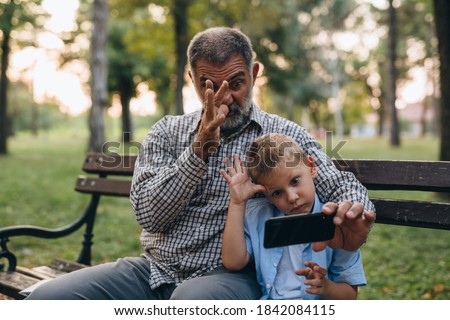grandfather with his grandson using mobile phone while sitting on bench in park